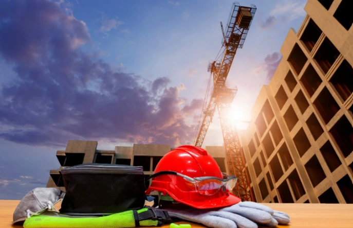 Hard hat, gloves and safety gear in front of a building under construction at sunset