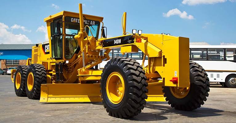 Yellow motor grader parked on a paved yard